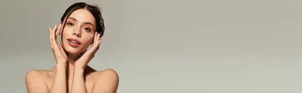 Una mujer joven y hermosa con la piel radiante toca suavemente su rostro, exudando confianza y gracia. - foto de stock