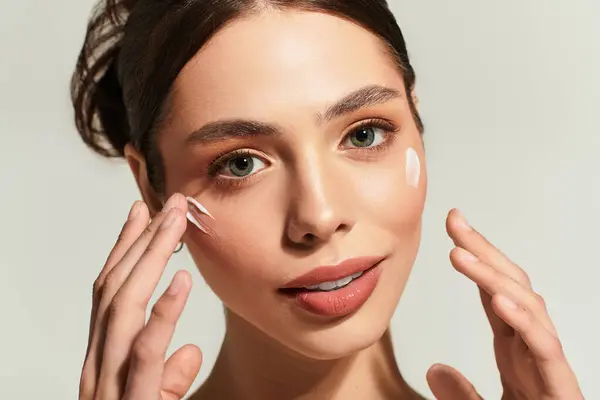 A beautiful woman applies cream to her face, revealing her glowing skin and happy smile. — Stock Photo