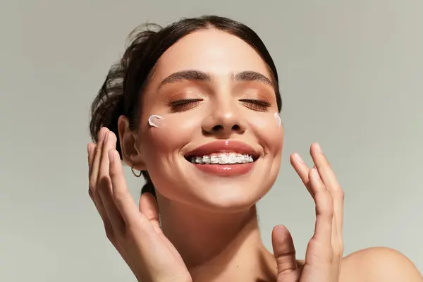 Joyful woman applies cream to her face, radiating positivity in a clean backdrop. — Stock Photo