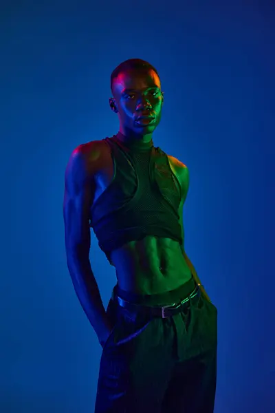 A confident young african american man stands stylishly in bright lights, showcasing urban fashion. — Stock Photo
