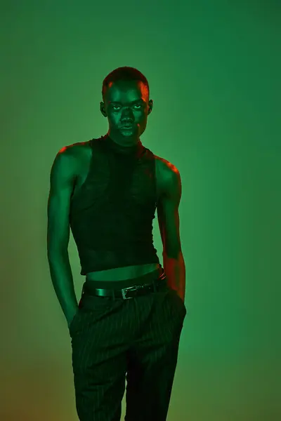 A young african american man exudes charisma in trendy attire, illuminated by dynamic green hues. — Stock Photo