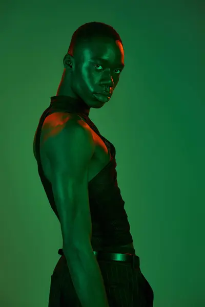A confident young man dressed in fashionable attire stands against a striking green backdrop. — Stock Photo