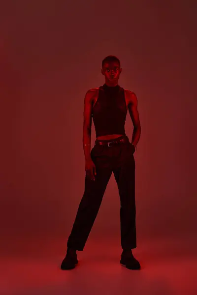 A young african american man displays his stylish outfit against a bold red backdrop, radiating confidence. — Stock Photo