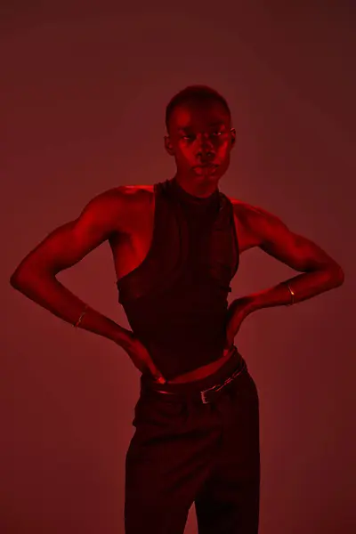 Young man in modern fashion stands against a red backdrop, exuding confidence and style. — Stock Photo