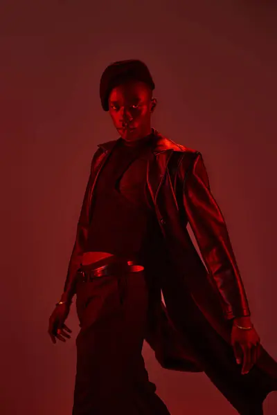 Stylish young man showcases confidence and flair in a red lit backdrop, embodying modern fashion. — Stock Photo