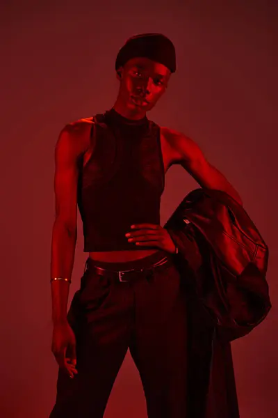 A young man in a stylish outfit stands confidently against a dramatic red backdrop. — Stock Photo