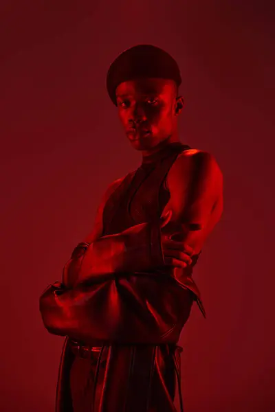 A young african american man shows off his stylish outfit with confidence in a vibrant red backdrop. — Stock Photo