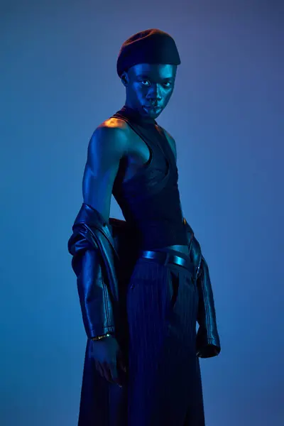 Un joven afroamericano muestra con confianza su elegante atuendo con cautivadora luz azul. - foto de stock