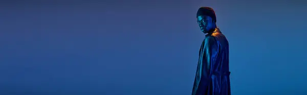 Молодий афроамериканський чоловік у стильному, яскравому одязі впевнено стоїть на тлі синього фону. — стокове фото