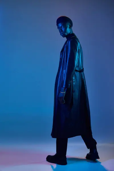 A young african american man stands confidently in stylish attire, lit by vibrant blue and purple lights. — Stock Photo