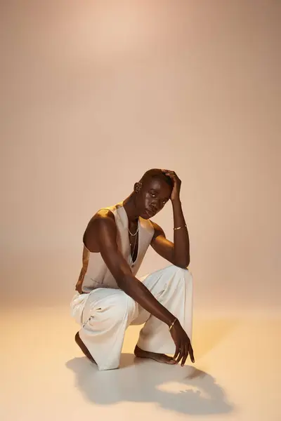A vibrant young african american man in stylish attire squats in a minimalist studio. — Stock Photo