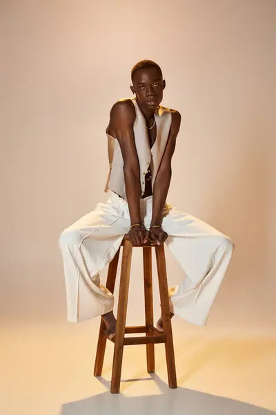 Un giovane uomo afroamericano siede su uno sgabello di legno, ostentando il suo vestito elegante e vibrante energia. — Foto stock