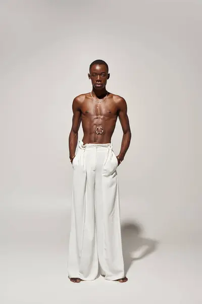 Un giovane uomo afroamericano fiducioso posa in eleganti pantaloni bianchi, in mostra la moda moderna. — Foto stock