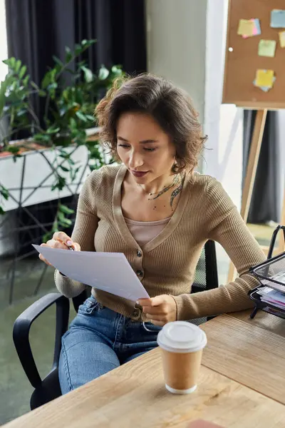 Une jeune femme passe en revue des notes lorsqu'elle est assise à un bureau en bois dans un environnement de bureau lumineux. — Photo de stock