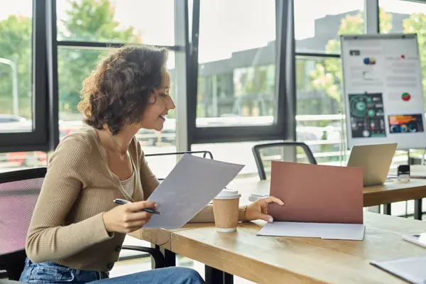 A woman engages in thoughtful work at her desk, surrounded by modern office elements and greenery. — Stock Photo