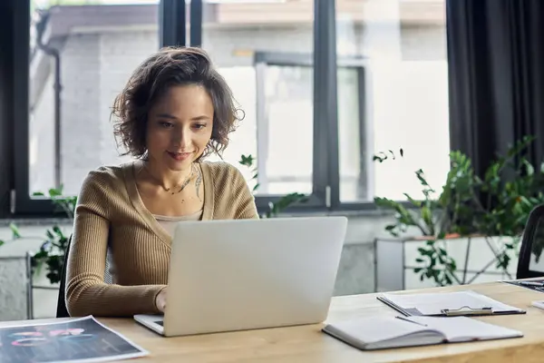 Individuo dedicato naviga senza sforzo il suo computer portatile in uno spazio di lavoro luminoso e verde durante il giorno. — Foto stock