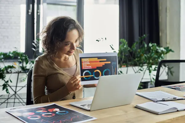 A woman engaged in a work session is presenting charts on a digital device while seated at a desk. — Stock Photo