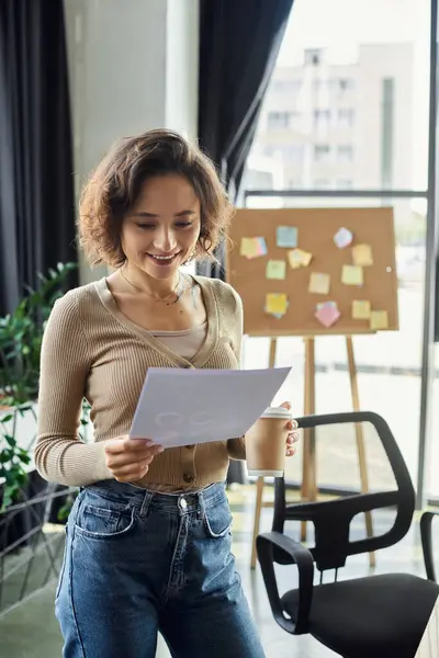 Une femme motivée se tient dans un bureau chic, sirotant du café et examinant des documents importants. — Photo de stock