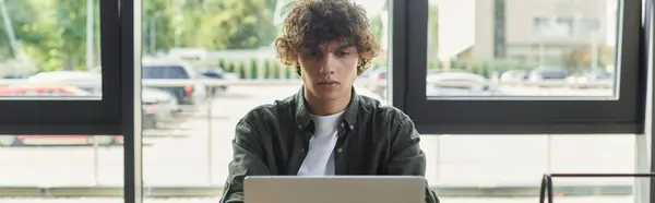 Young person with curly hair concentrated on their laptop in a bright office environment. — Stock Photo