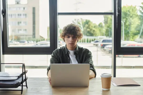 A young person sits at a desk, focused on their laptop while sipping coffee. — Stock Photo
