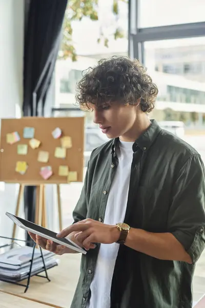 A young professional focuses intently on their tablet, surrounded by a vibrant office atmosphere. — Stock Photo