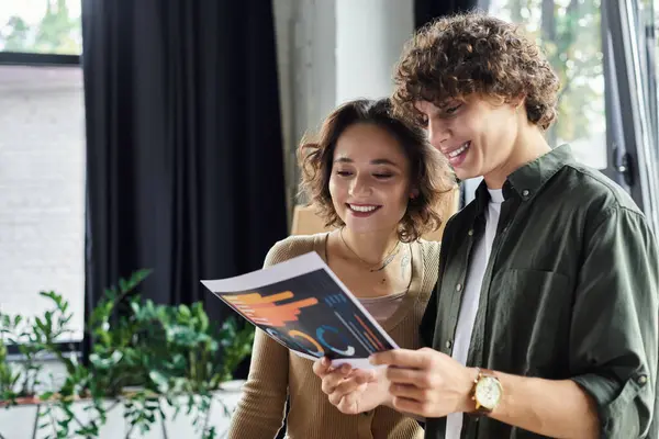 Two colleagues share ideas while reviewing colorful documents in a modern office setting. — Stock Photo