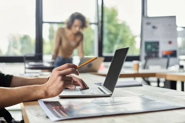 A person types on a laptop while another stands nearby, engaged in a collaborative work effort. — Stock Photo