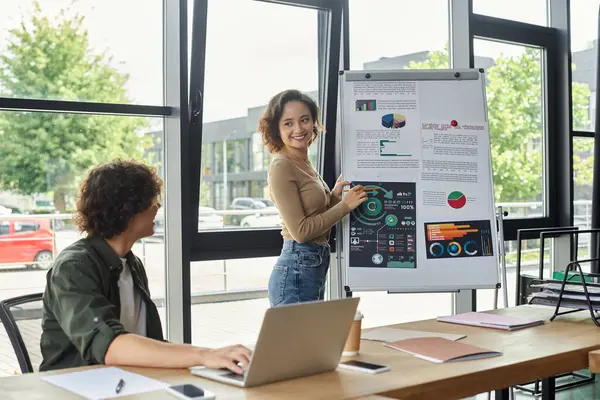 A woman stands by a presentation board in a bright office, engaging her colleague during a meeting. — Stock Photo