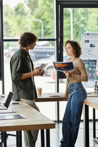 Two colleagues discuss ideas while surrounded by documents and modern office equipment in daylight. — Stock Photo