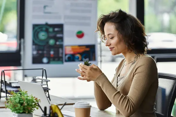 Young professional focuses on a small plant while working diligently at a stylish office desk. — Stock Photo
