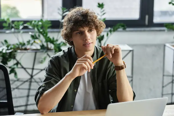 Un giovane uomo si siede ad una scrivania in un ufficio moderno, pensando ai suoi prossimi passi con una matita. — Foto stock