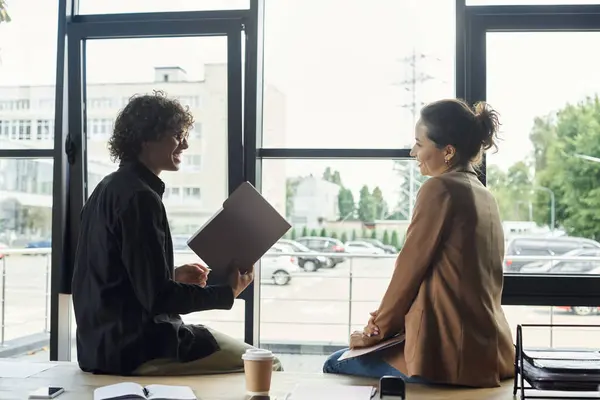 Two coworkers discuss concepts and projects near large windows in the office. — Stock Photo