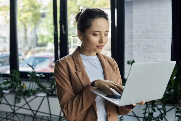 A focused individual types on a laptop in a bright office brimming with greenery. — Stock Photo