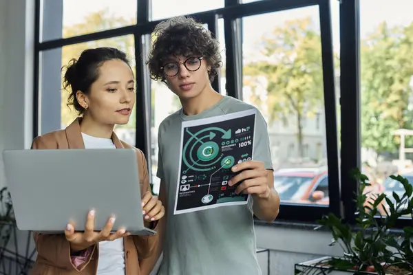Two young professionals engage in an inspiring discussion while reviewing a document and laptop. — Stock Photo