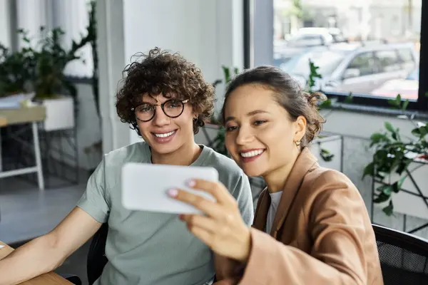 Zwei Kollegen genießen einen unbeschwerten Moment, während sie gemeinsam im Büro ein Selfie machen. — Stockfoto