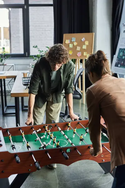 Two colleagues enjoy a competitive game of foosball during their break in a lively office setting. — Stock Photo