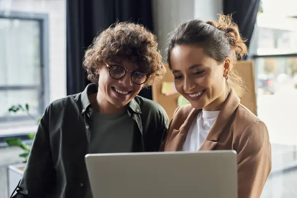 Two colleagues excitedly share ideas over a laptop in a bright office. — Stock Photo