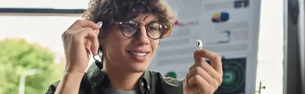 Curly haired person with glasses uses wireless earbuds in a creative, vibrant workspace. — Stock Photo