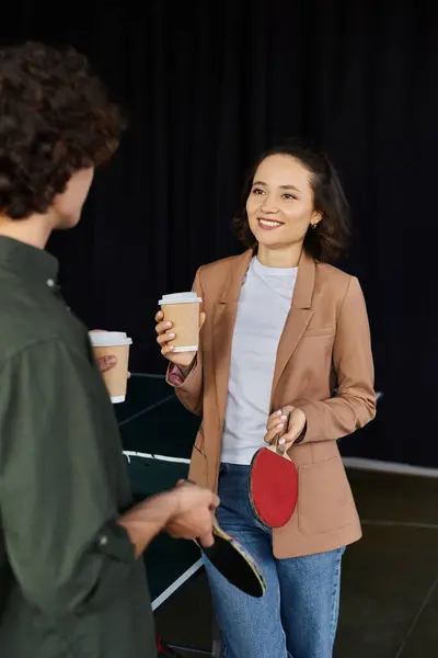 Zwei Kollegen unterhalten sich angeregt, während sie Kaffeetassen und Tischtennispaddeln im Büro halten.. — Stockfoto