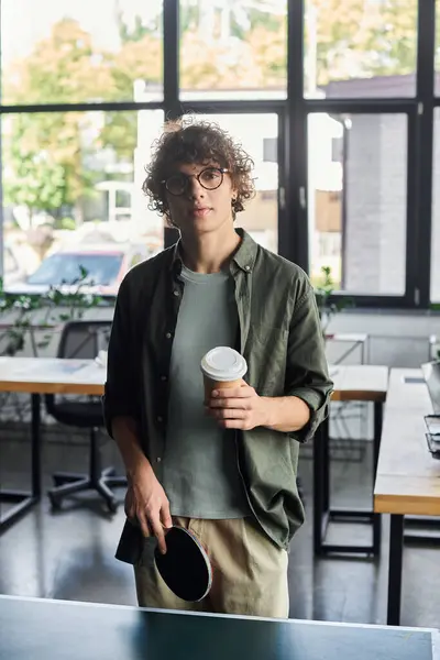 A young man pauses in a stylish office, sipping coffee and enjoying the calm atmosphere. — Stock Photo