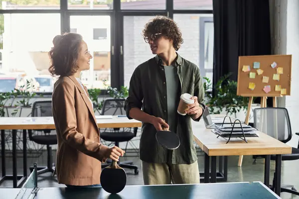 Two colleagues enjoy a lighthearted moment while playing table tennis in a vibrant office setting. — Stock Photo