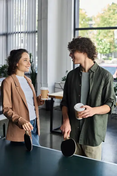 Zwei Kollegen teilen sich einen leichten Moment, während sie Getränke und Paddel in einem pulsierenden Bürozentrum halten. — Stockfoto