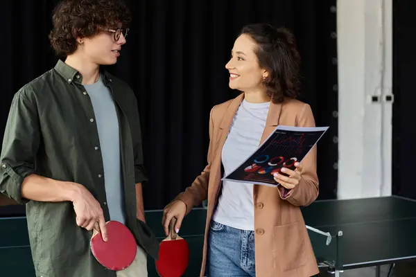 Two coworkers enjoy conversation while holding paddles and discussing table tennis at the office. — Stock Photo