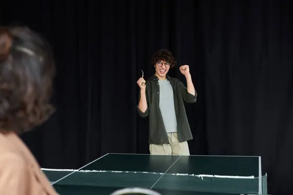 Una persona celebra un punto vinto durante una partita di ping pong in ufficio, mettendo in mostra il lavoro di squadra e il divertimento. — Foto stock