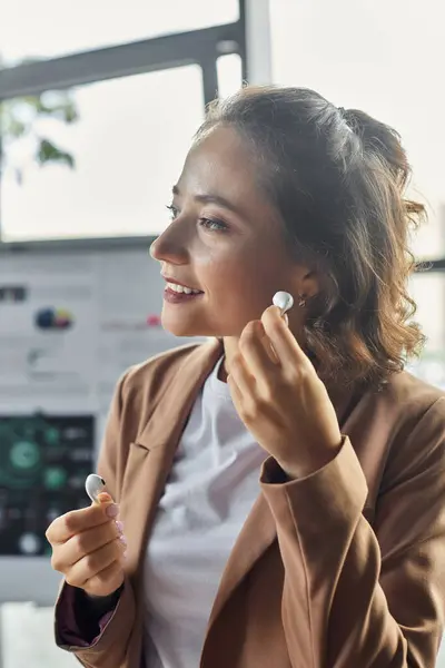 A focused individual adjusts their wireless earbuds while working in a bright office setting. — Stock Photo