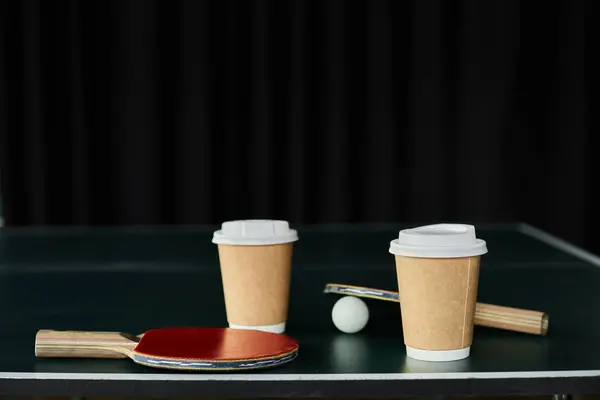 Kaffeetassen sitzen neben Tischtennispaddeln und einem Ball und schaffen eine lebendige Spielatmosphäre. — Stockfoto