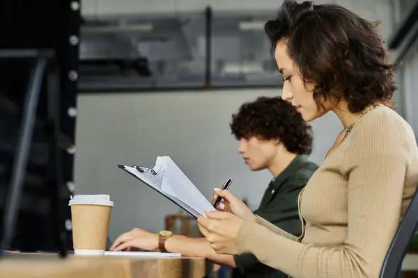 Dos personas dedicadas se dedican a tareas de trabajo, intercambiando ideas y notas en una oficina de invitación. - foto de stock