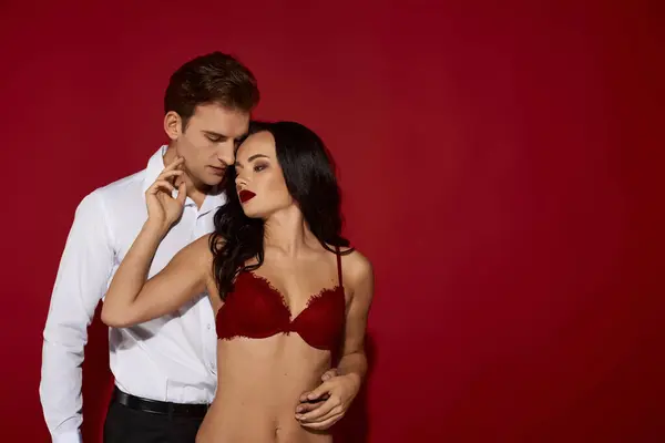 A couple embraces in front of a vivid red backdrop, capturing a moment of love. — Stock Photo