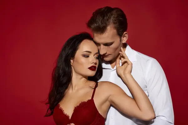 Um casal está perto, exalando amor e paixão contra um cenário vermelho arrojado. — Fotografia de Stock