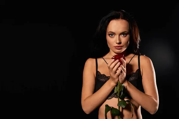 A charming young woman holds a rose gracefully in a dimly lit space. — Stock Photo